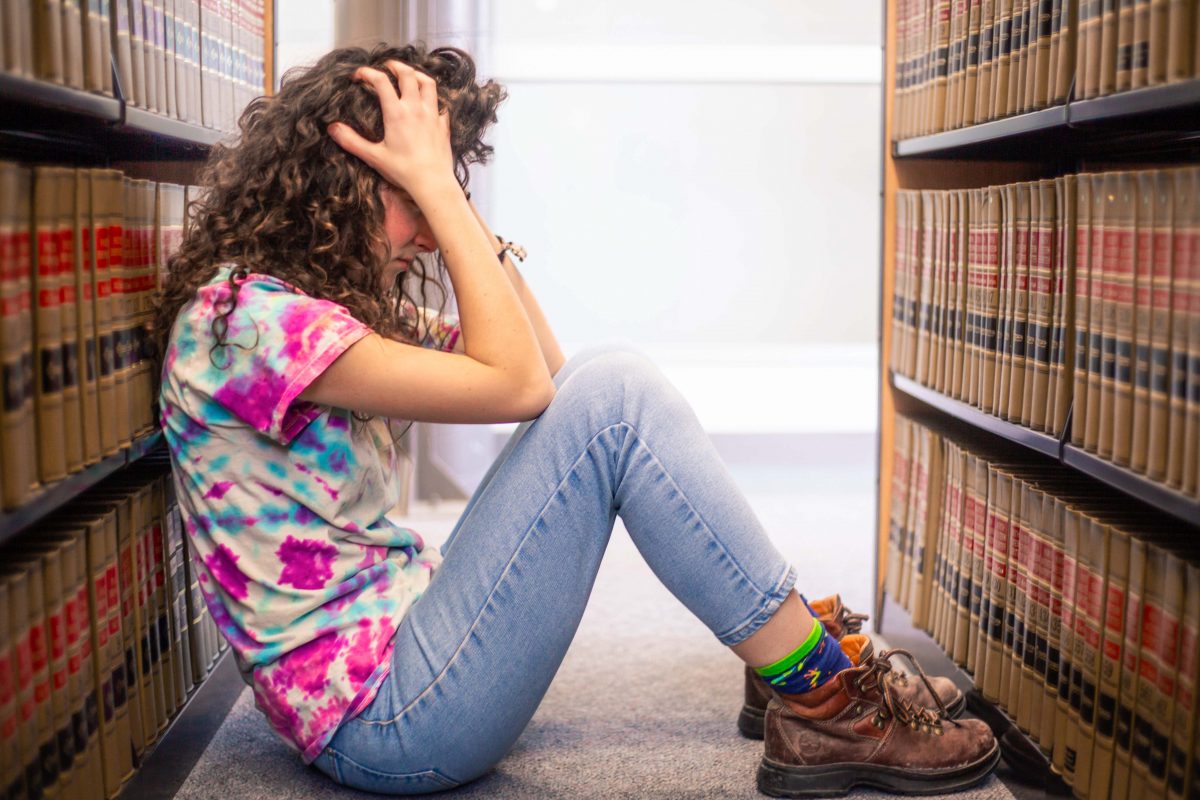stressed person sitting between book stacks, tie dye shirt, head in hands