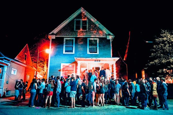 nighttime shot of people setanding outside an old house during a house party
