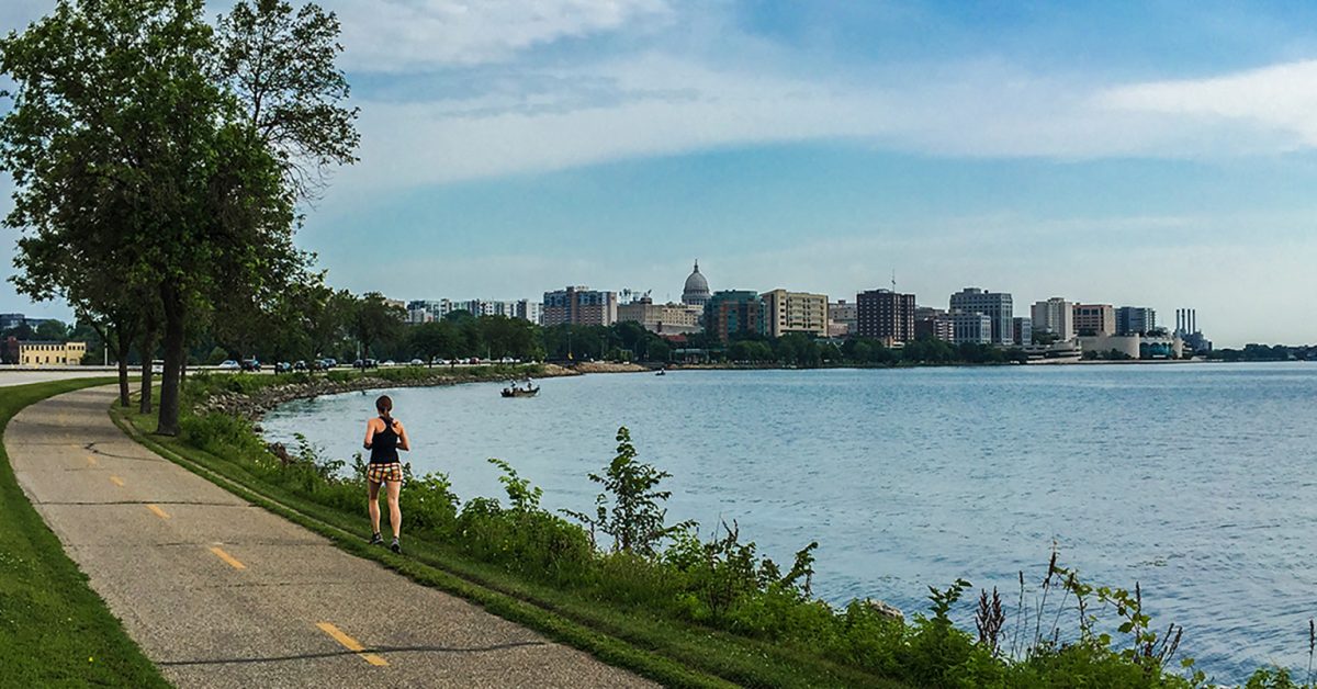 shoreline of madison showing lake monona and a runner on the side of the bikepath, capital in the background