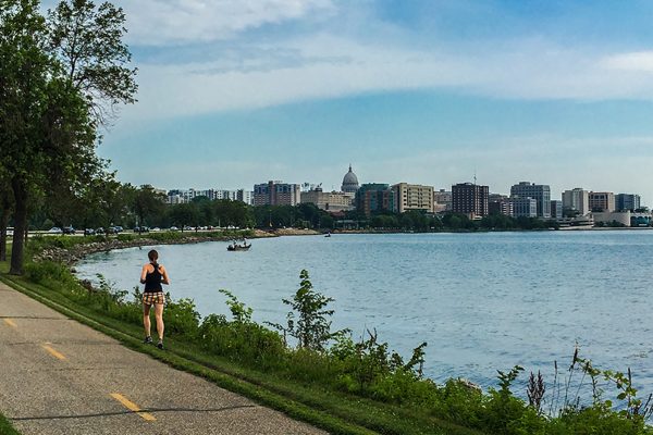 shoreline of madison showing lake monona and a runner on the side of the bikepath, capital in the background