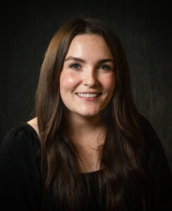 Anna Gorman is a female smiling in a black shirt with long brown hair.
