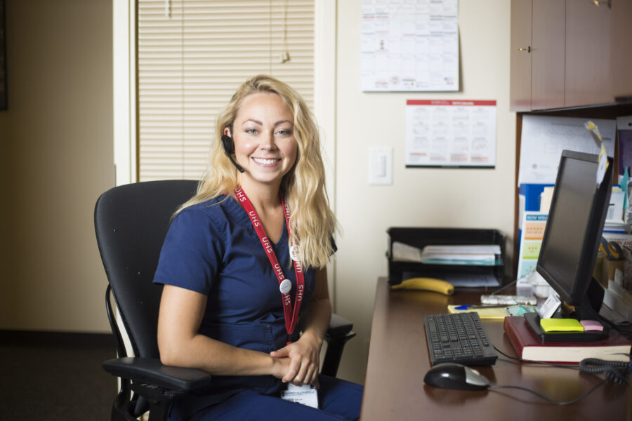 A nurse smiling from her desk wearing a headset.
