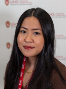 A woman with long black hair wearing a brown sweater and a read UHS lanyard.