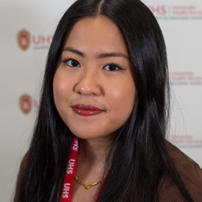 A woman with long black hair wearing a brown sweater and a read UHS lanyard.