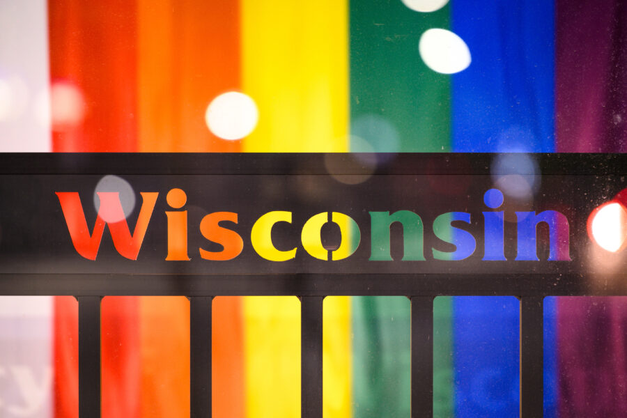 The side of a bus shelter window with the word Wisconsin, a rainbow pride flag in the background.