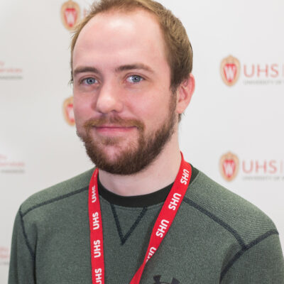 Brandon Juno has brown hair, a beard, and is wearing a green shirt.