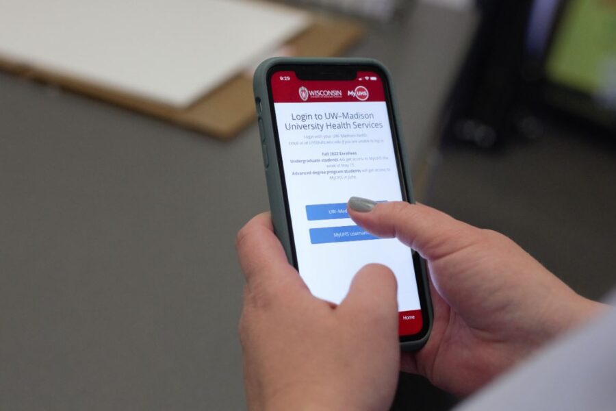 Two hands are holding an iphone with the MyUHS log in screen visible.