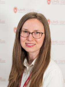 A women has long brown hair, is wearing glasses and a white shirt.