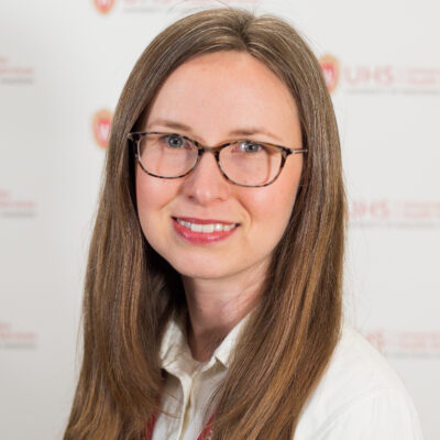 A women has long brown hair, is wearing glasses and a white shirt.