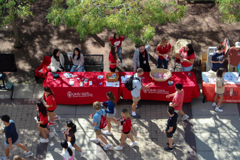 Students walk past UHS tables at an outdoor event on East Campus Mall.