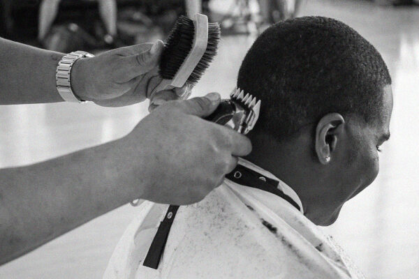 Black and white close up of a barber shaving a student's head.
