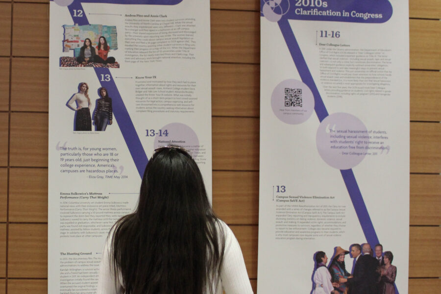 A person stands in front of two banners detailing campus sexual assault activism history.