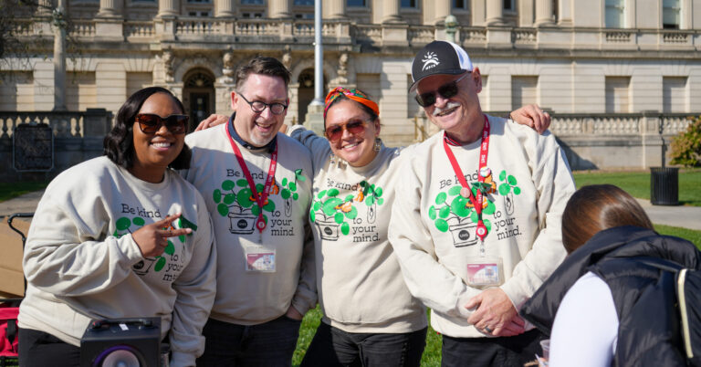 Four mental health providers in matching beige sweatshirts stand smiling together in front on Library Mall
