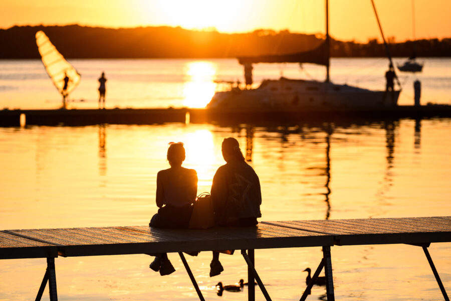 People in silhouette sit along the Lake Mendota shoreline and piers at the Memorial Union Terrace at the University of Wisconsin-Madison and watch the sun set during late spring/early summer on June 14, 2021