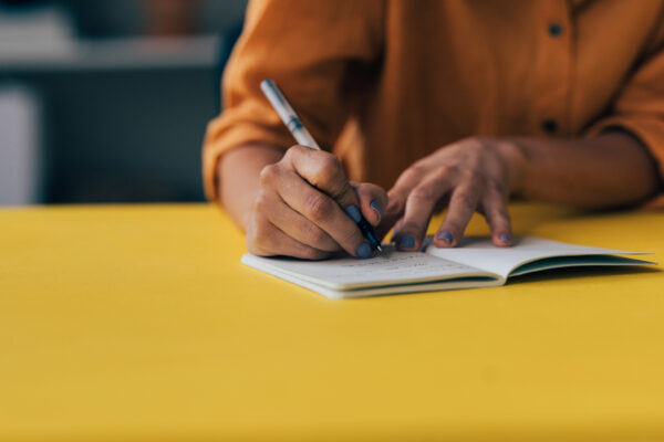 Someone writing in a notebook on a yellow table