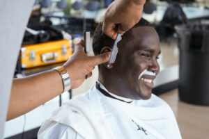 Male smiling as he gets haircut. Shaving cream on upper lip.