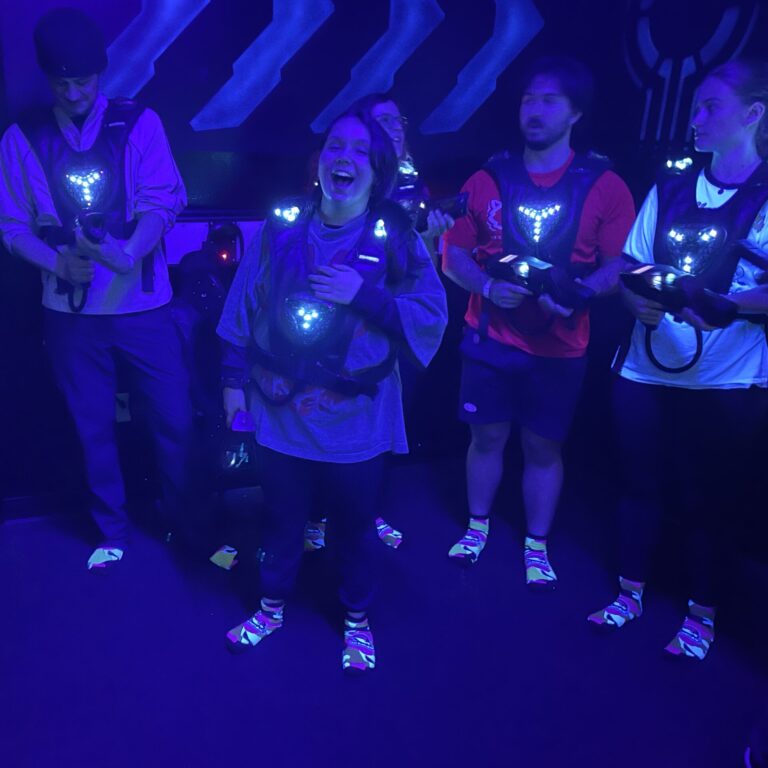 A group of people with laser tag vests standing under blacklights