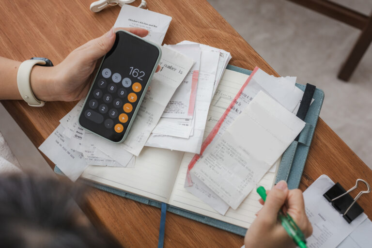 Person holding calculator above papers and a notebook while writing