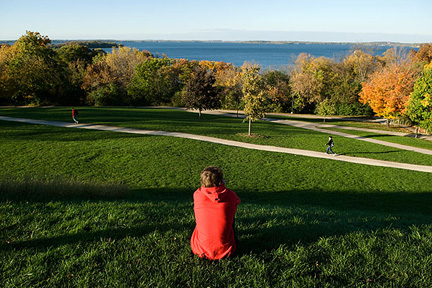 Person with a red shirt sitting in grass on Observatory Hill looking out at Lake Mendota
