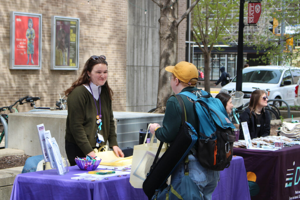 Student speaking with a representative of an off campus organization at tabling event outside for Sexual Assault Awareness Month.
