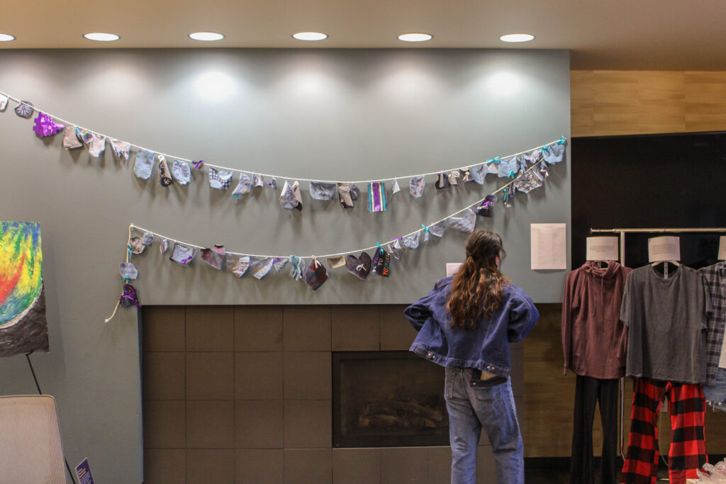 Person viewing art gallery pieces including pieces of clothing, community arts project, and a large piece of art.