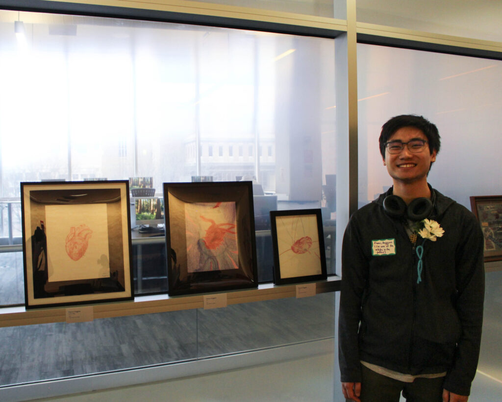 Student posing and smiling with their art submitted to the Reflect Art Gallery.