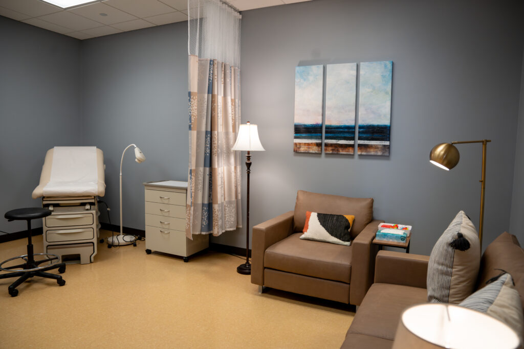 Sexual Assault Forensic Exam room in the Survivor Services suite. Two couches and a medical table are pictured.