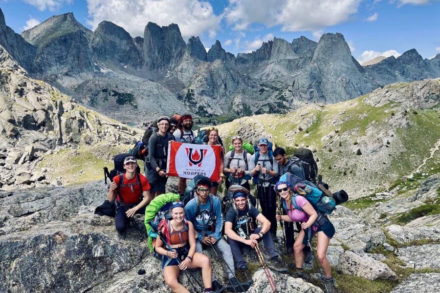 UW Hoofers students on standing in front of mountains smiling and holding their club flag.