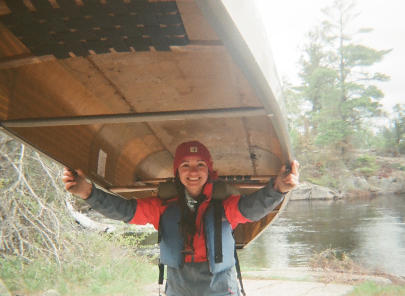 Rhiannon smiling while holding a canoe overhead.