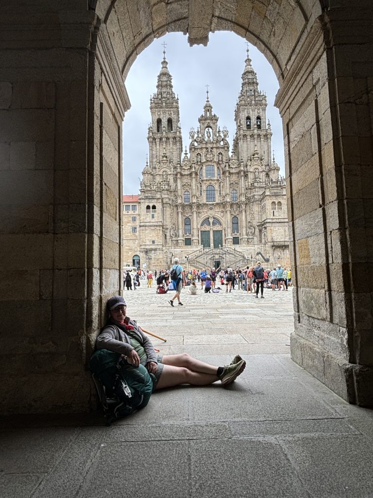 Sara Beachy Waters seated on the ground while traveling smiling with architecture in the background.