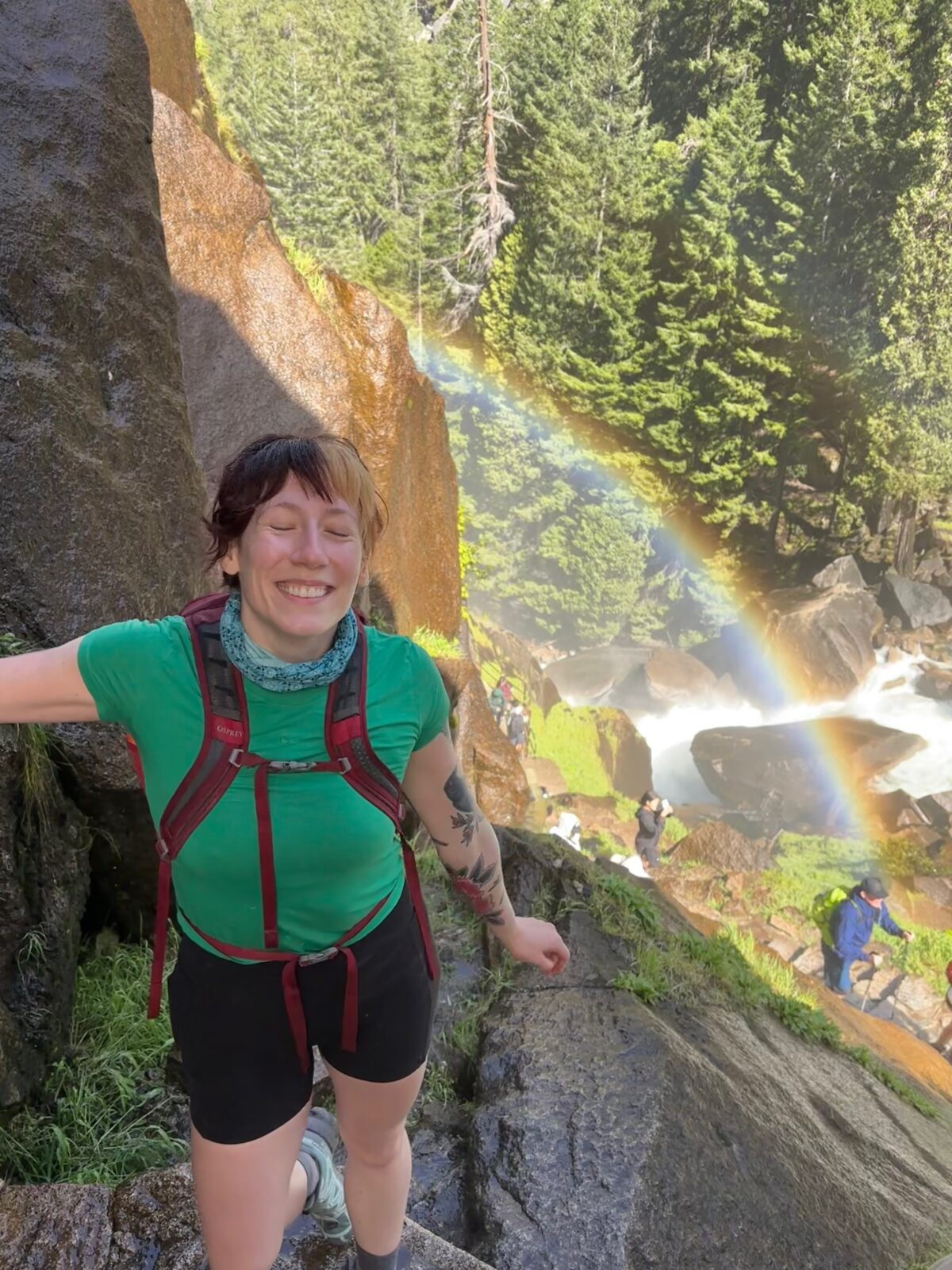 Bridgegt smiling on a hike with a rainbow in the background.