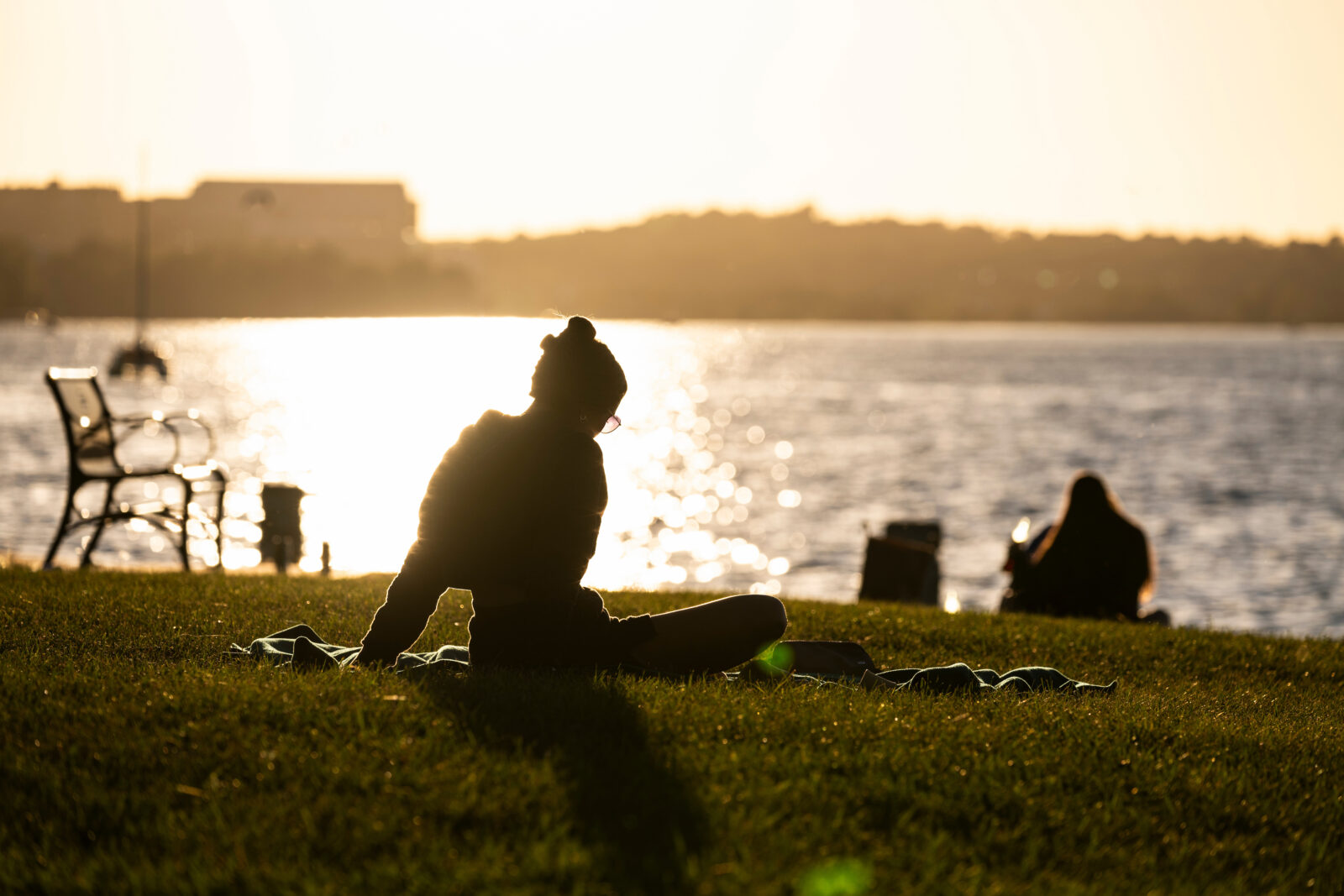 Person seated on a blanket in front of the lake.