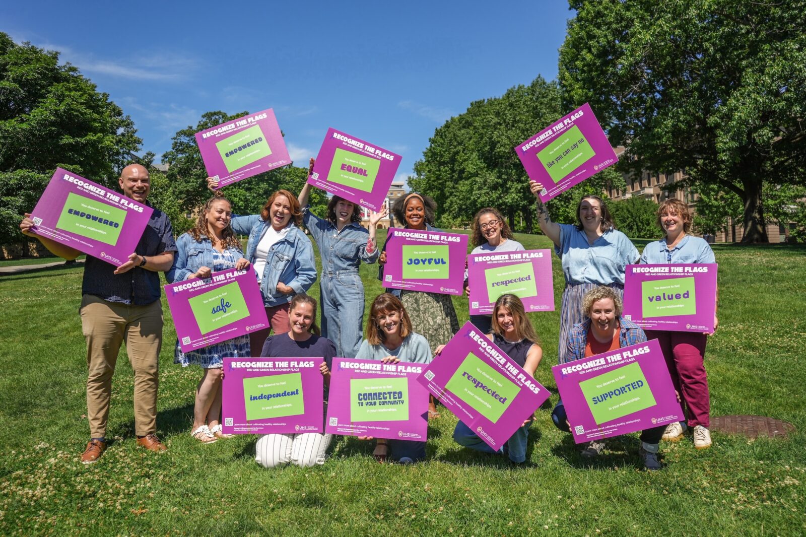 The Survivor Services team poses and smiles with various "green flag" reminder signs on Bascom Hill.