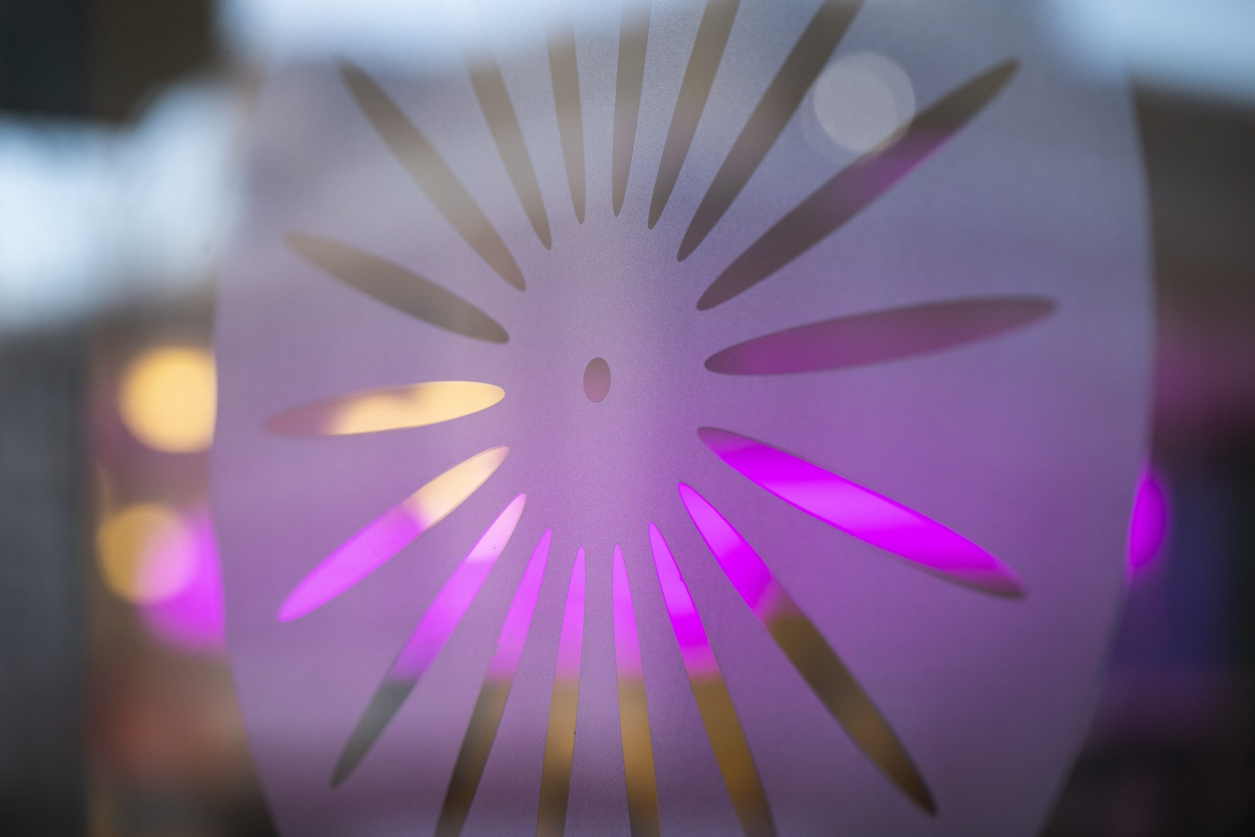 A frosted sunburst graphic of the iconic Memorial Union Terrace chair design is backlit by out-of-focus colored lights in the background of a glass entry door to the Memorial Union